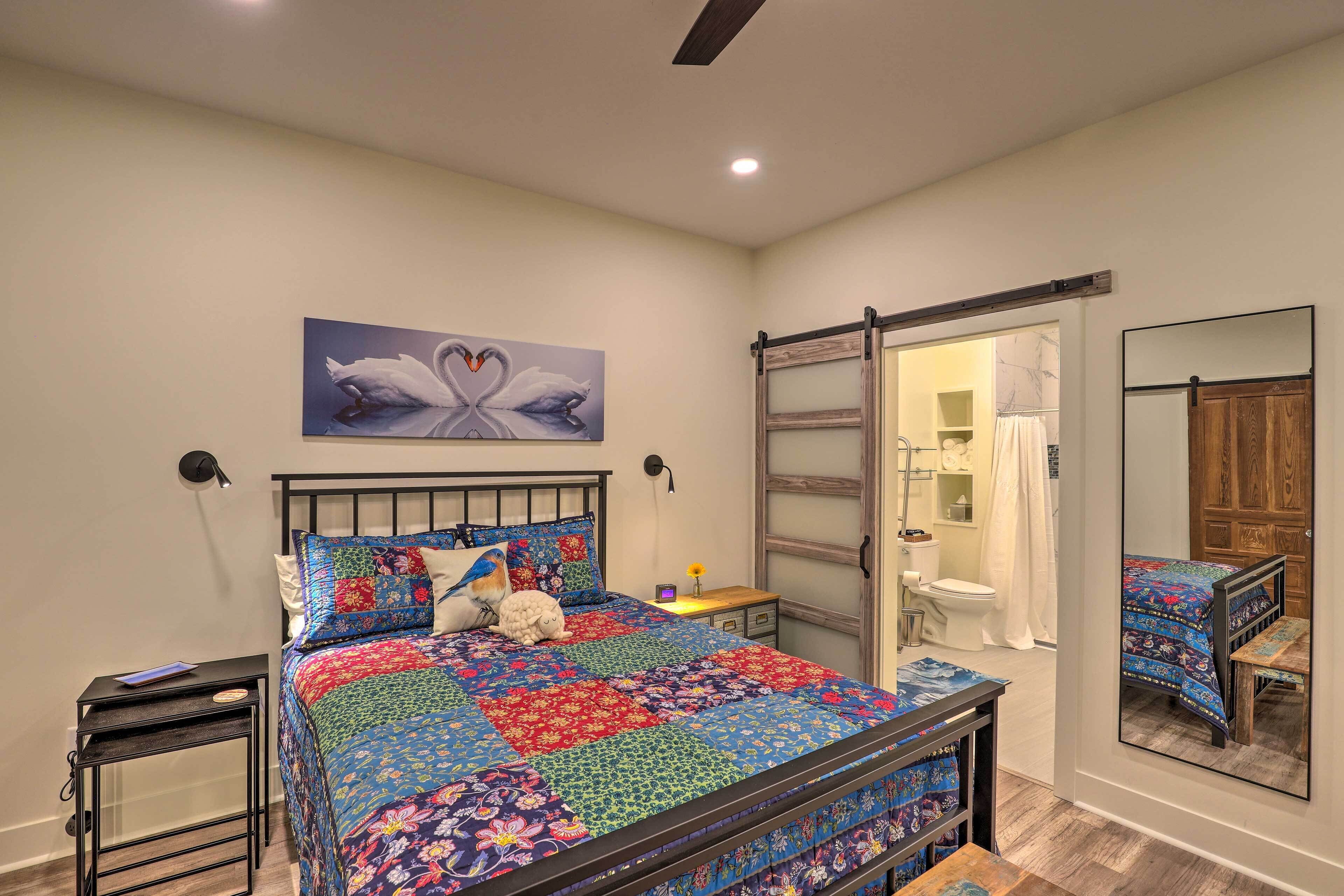 A bedroom with a bed, a nightstand, a wall-mounted lamp, a mirror, and a sliding door leading to a bathroom.