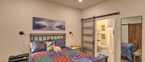 A bedroom with a bed, a nightstand, a wall-mounted lamp, a mirror, and a sliding door leading to a bathroom.