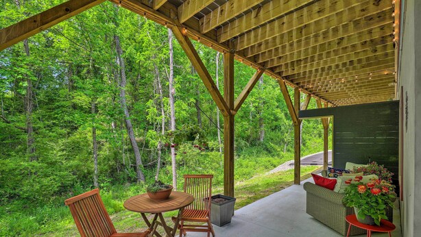 Une terrasse couverte, meublée de meubles en bois, agrémentée d’une plante en pot et offrant une vue sur une forêt.