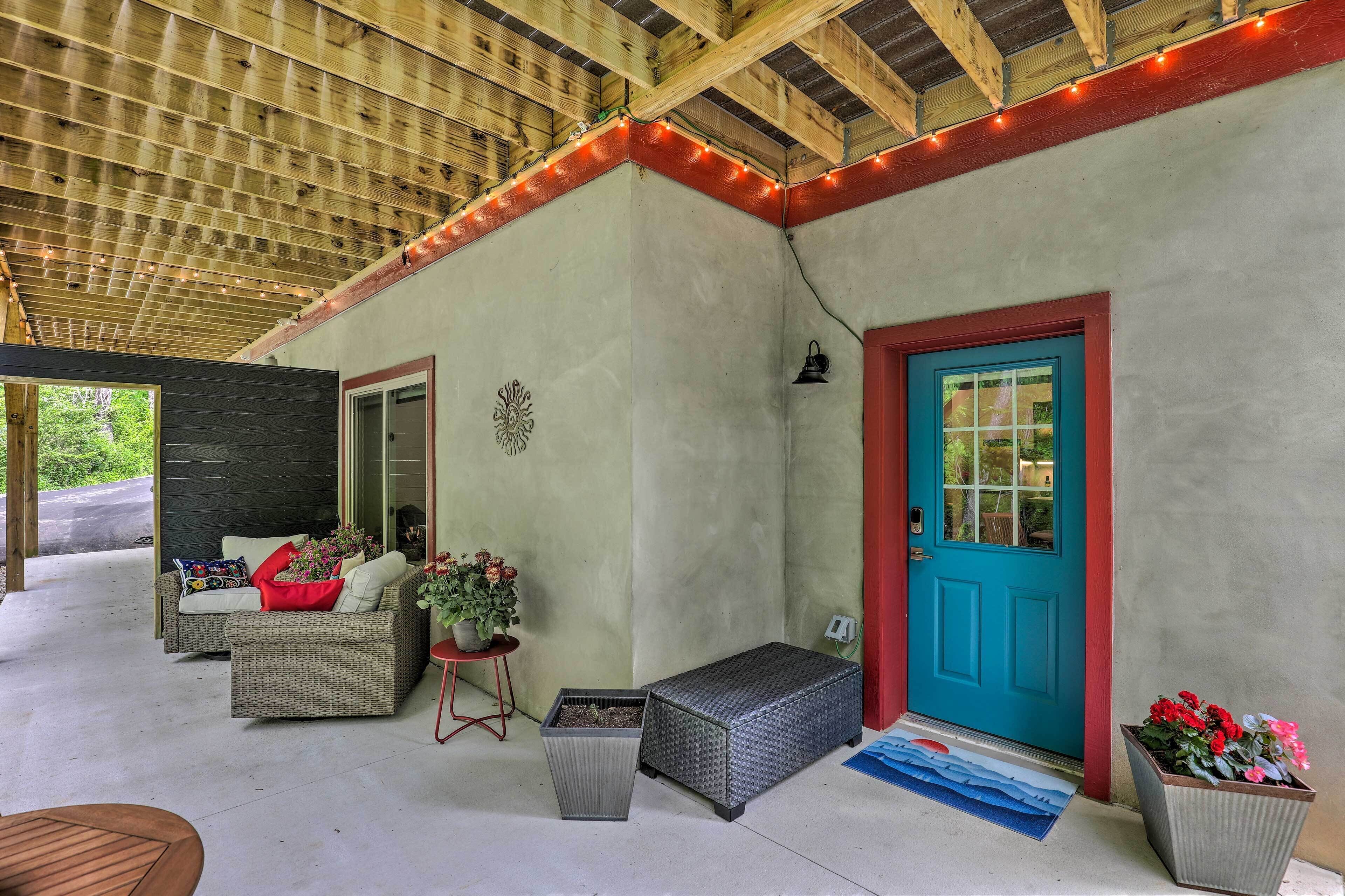 A covered porch with wicker furniture, a blue door, and potted plants.