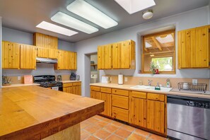 A kitchen with wooden cabinets, a large island, a stove, a dishwasher, and a window with a view.