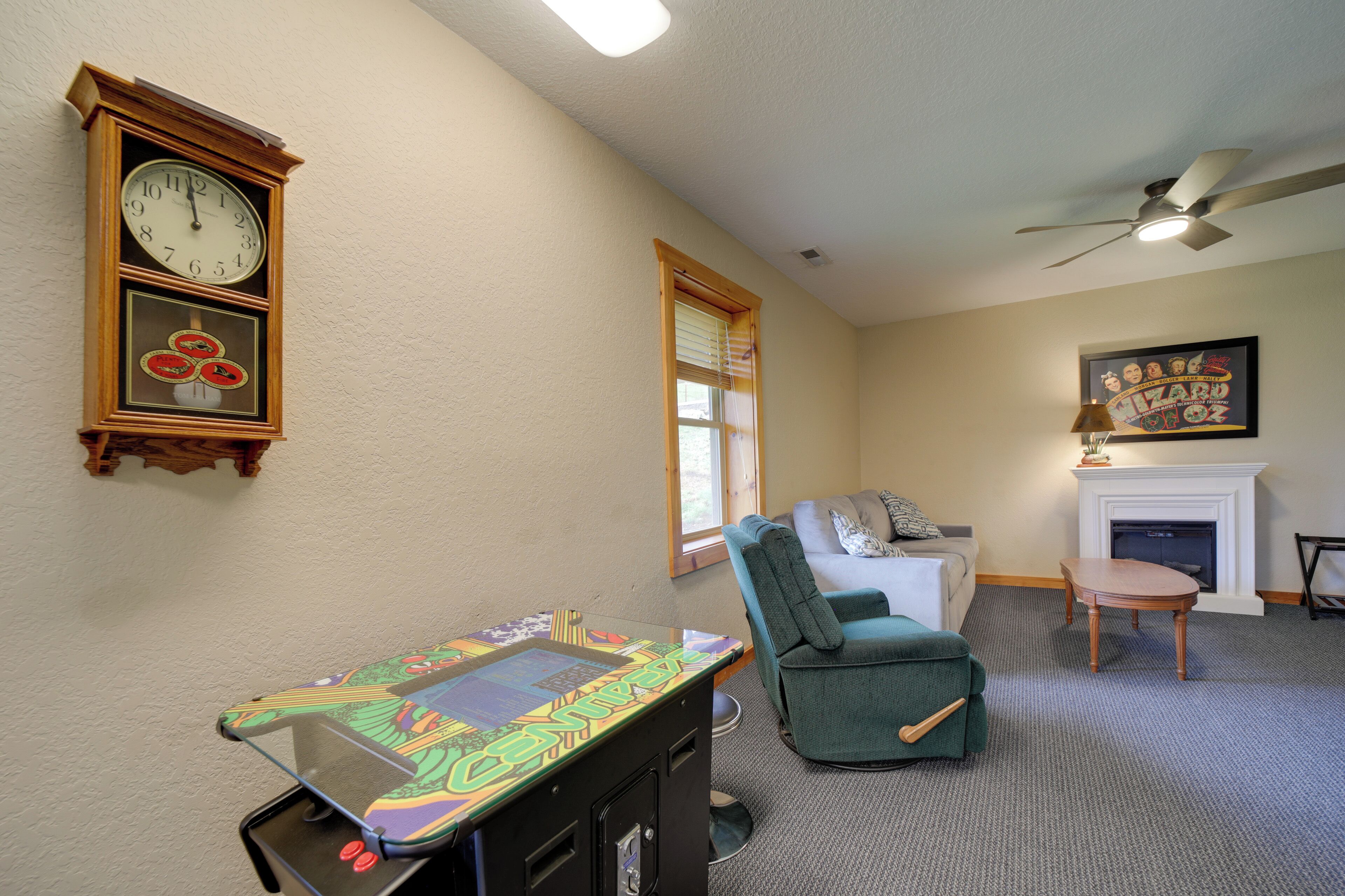 Une pièce avec une horloge, un fauteuil vert, une cheminée et un ventilateur de plafond.
