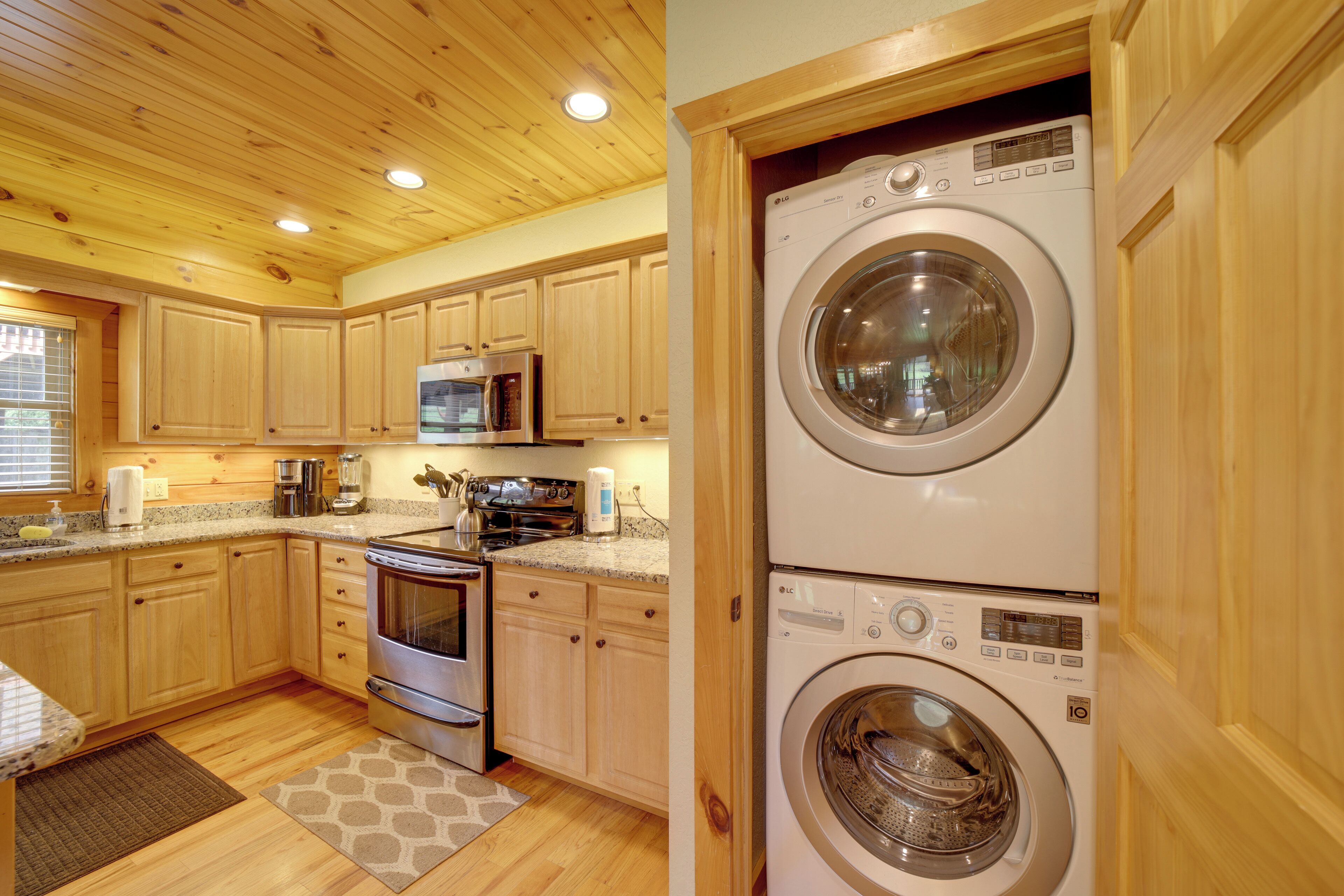 A compact kitchen with wooden cabinets, a microwave, an oven, and a washing machine.