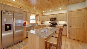 Eine Küche mit Holzausstattung, einem Edelstahlkühlschrank, Granit Arbeitsplatten und einer zentralen Kücheninsel mit Barhocker.