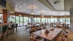 A spacious dining area with multiple tables and chairs, large windows, and a stone accent wall.