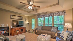 A living room with a ceiling fan, a large flat-screen TV, a sofa, ottomans, and a bookshelf.