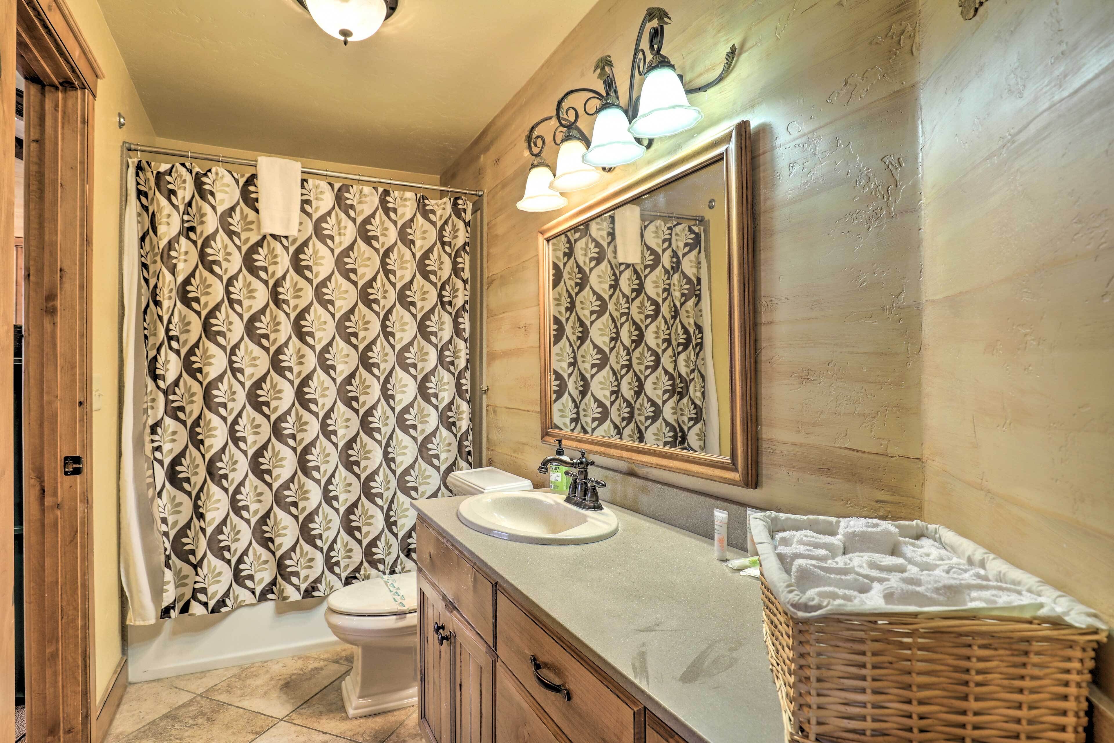 A bathroom with a patterned shower curtain, a sink, a mirror, and a wicker basket.