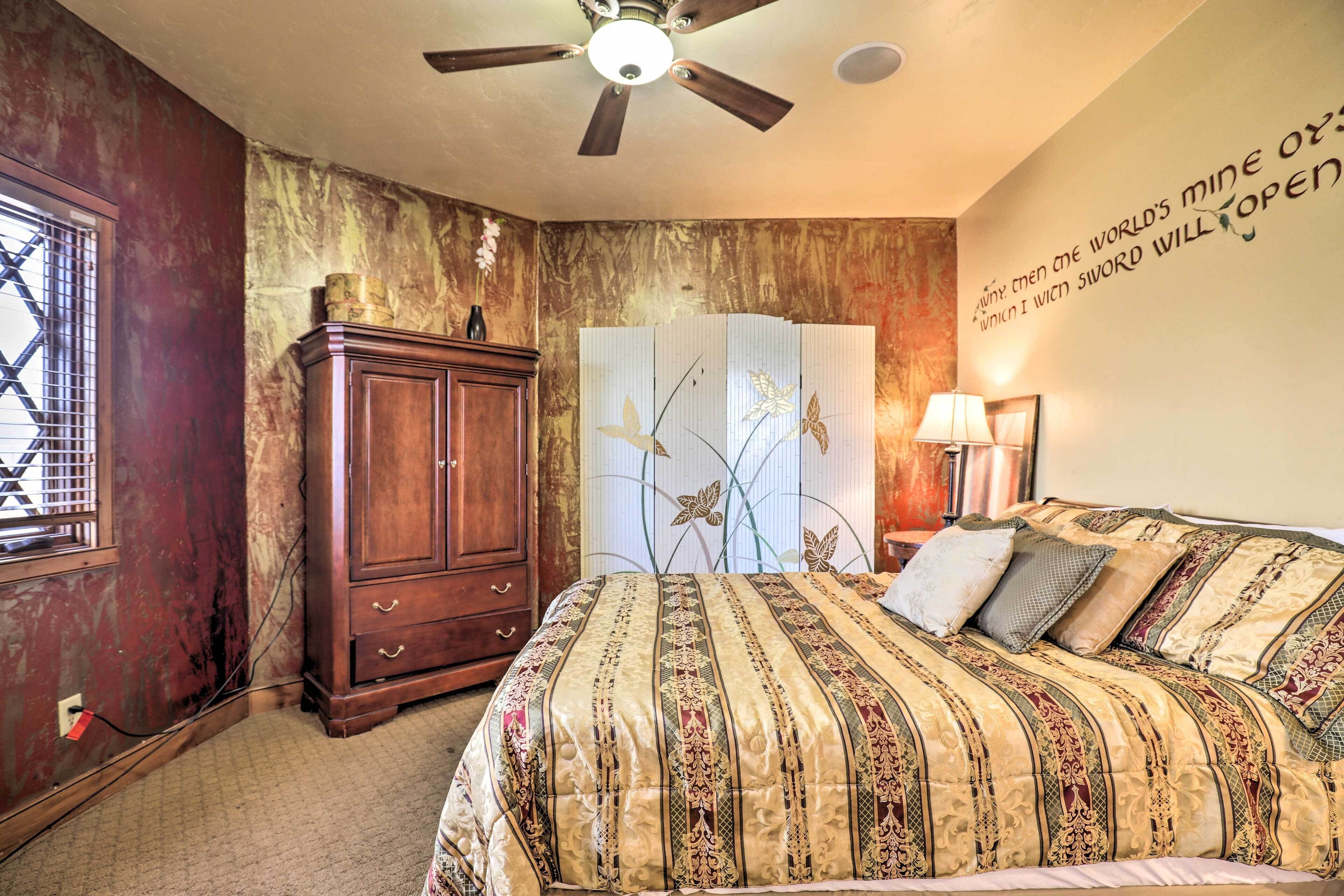 Un dormitorio con cama, ventilador de techo, armario de madera, pared decorativa con una cita y ventana con barrotes.