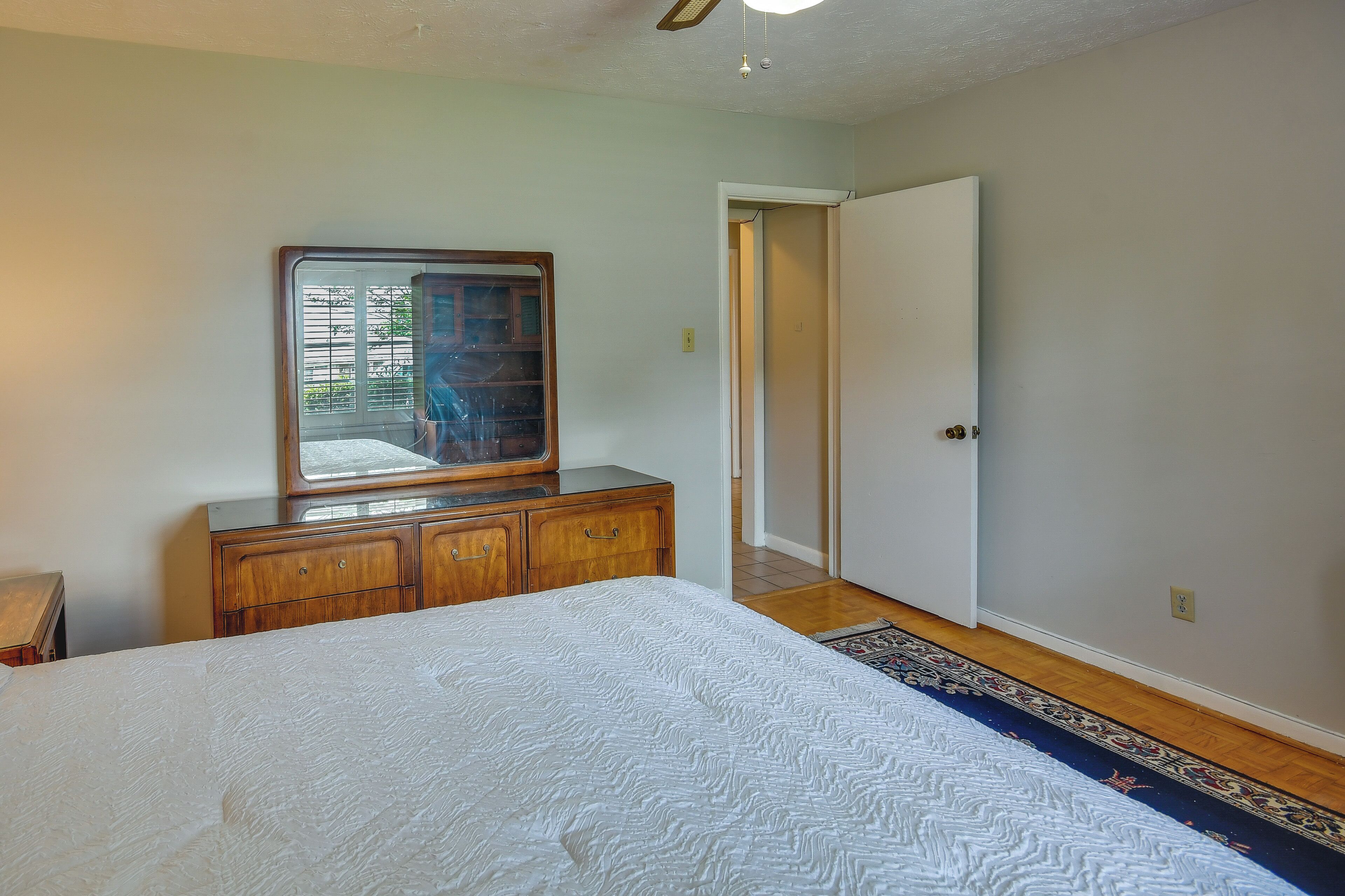 A bedroom with a bed, wooden dresser, mirror, and a door leading to another room.