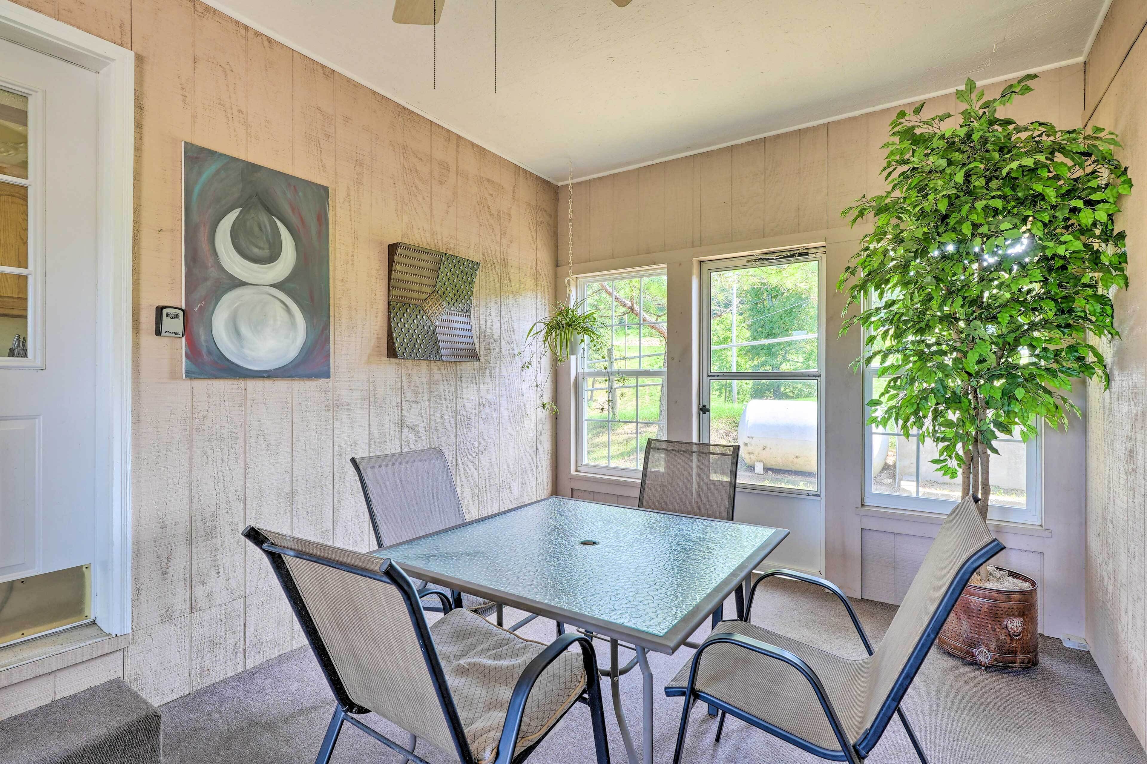 Une véranda avec une table en verre, des chaises, une plante en pot et des œuvres d’art accrochées aux murs.