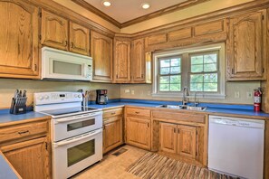 A kitchen with wooden cabinets, a white stove, a microwave, a dishwasher, and a window with a view of greenery.