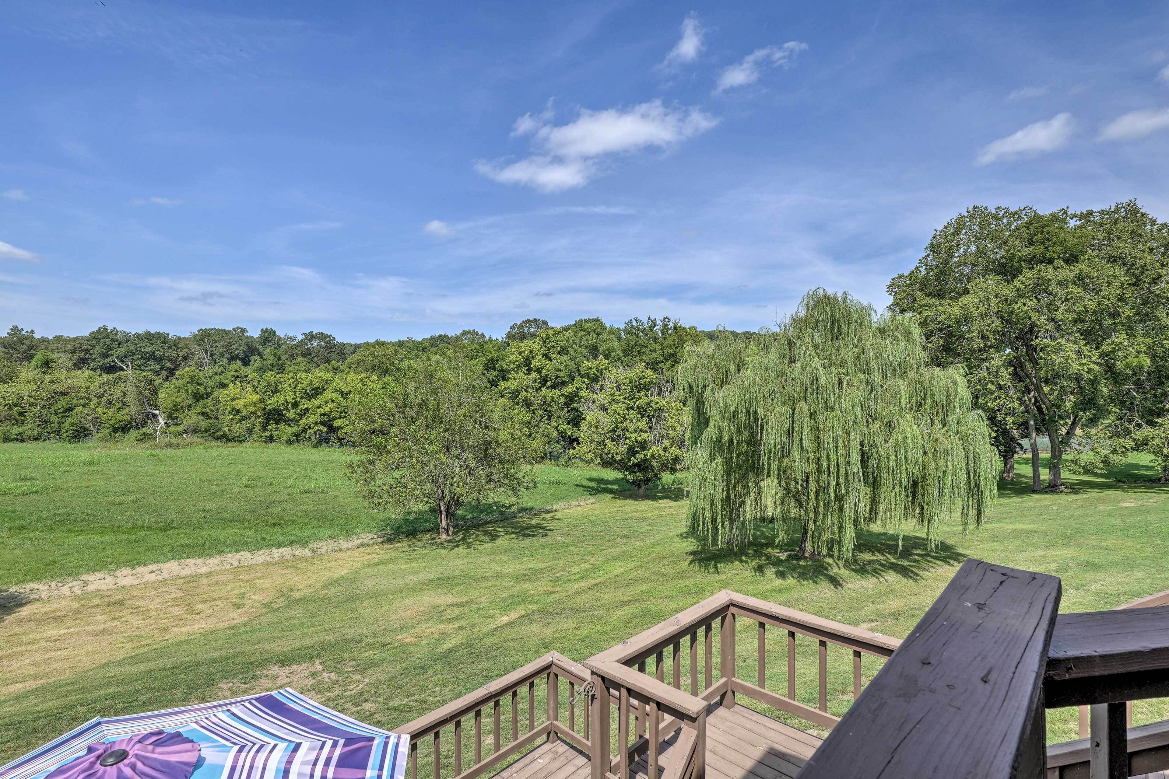 A wooden deck with a view of a grassy field and trees.
