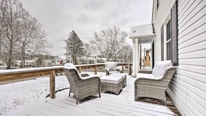 A covered porch with wicker furniture and a wooden railing, surrounded by snow-covered ground and trees.