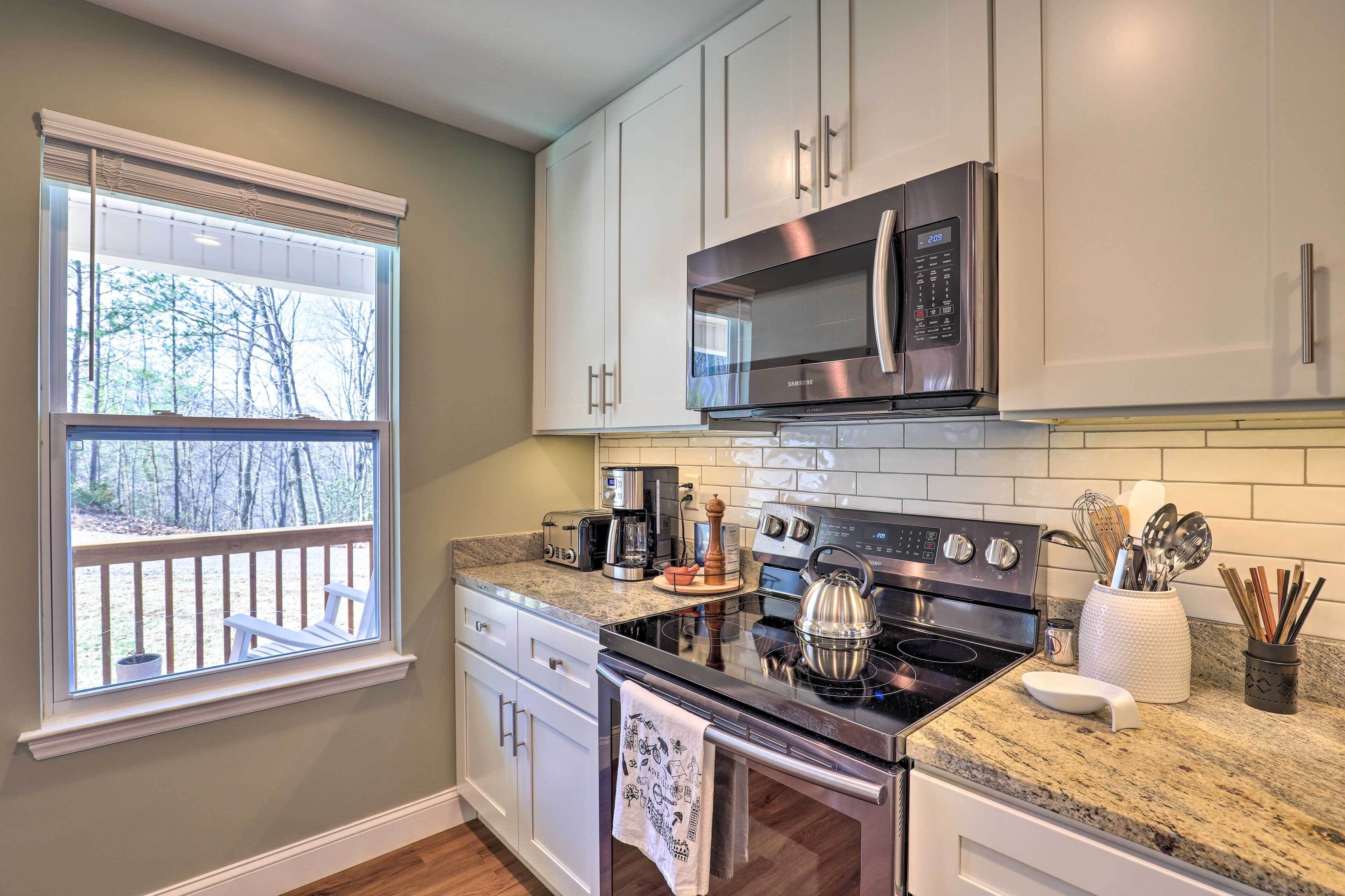 A kitchen with white cabinets, stainless steel appliances, and a window with a view of trees.