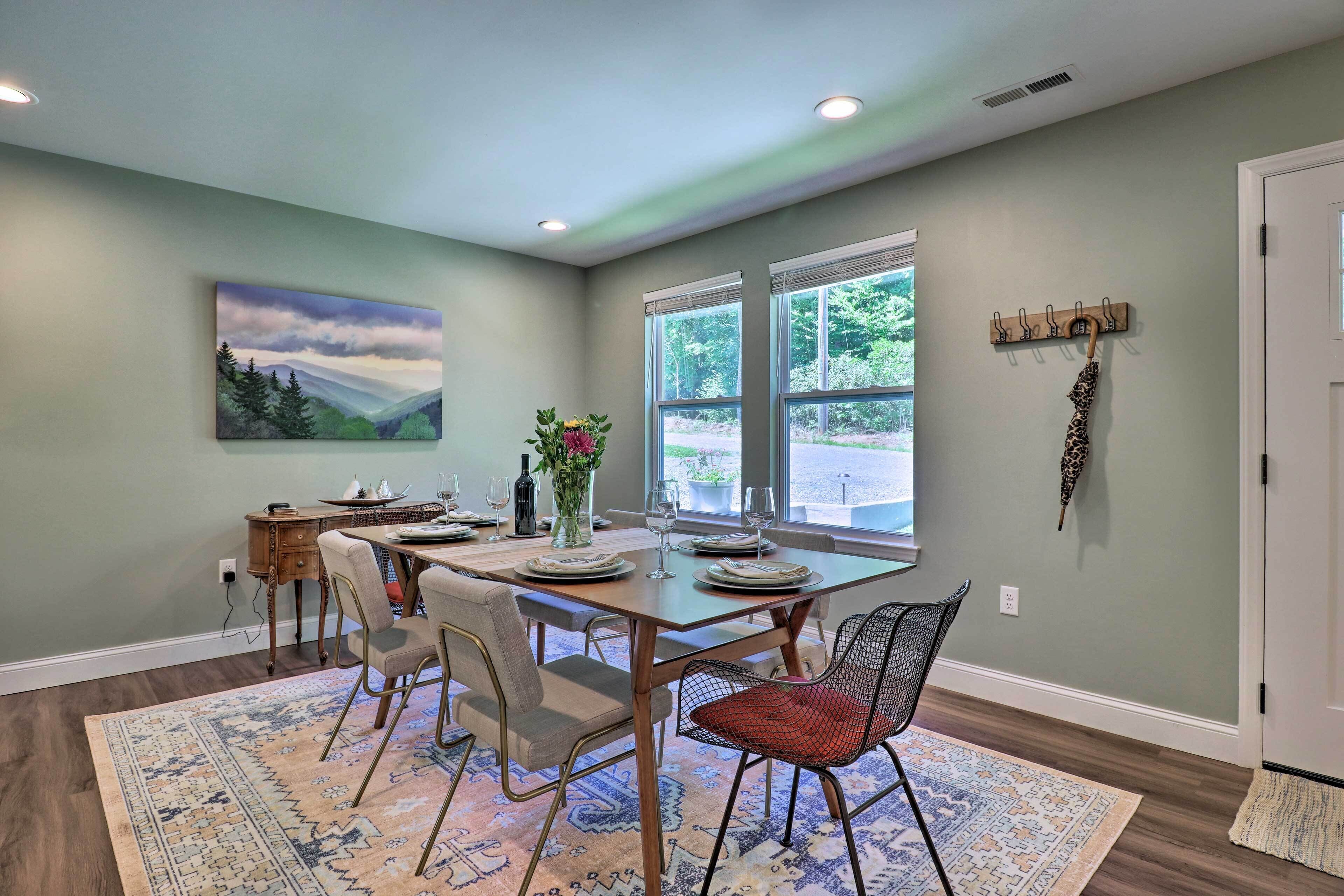 A dining area with a table set for four, a painting on the wall, and a coat rack.