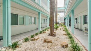 A building with a central courtyard featuring a palm tree, surrounded by a pathway with rocks and plants.