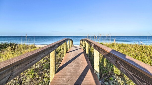 A wooden boardwalk leading to a beach with clear skies.