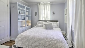 Une chambre à coucher avec un lit, une armoire blanche et une fenêtre avec des rideaux.