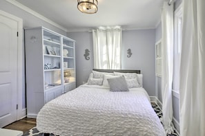 A bedroom with a large bed, a white wardrobe, and a window with sheer curtains. - Chincoteague Island Cottage ~ 2 Mi to Beaches (Chincoteague)