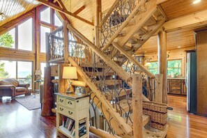 A spacious interior with a wooden staircase, a cozy seating area, and a view through large windows. - Panoramic Mtn Views: Luxe Cataloochee Cabin! (Waynesville)
