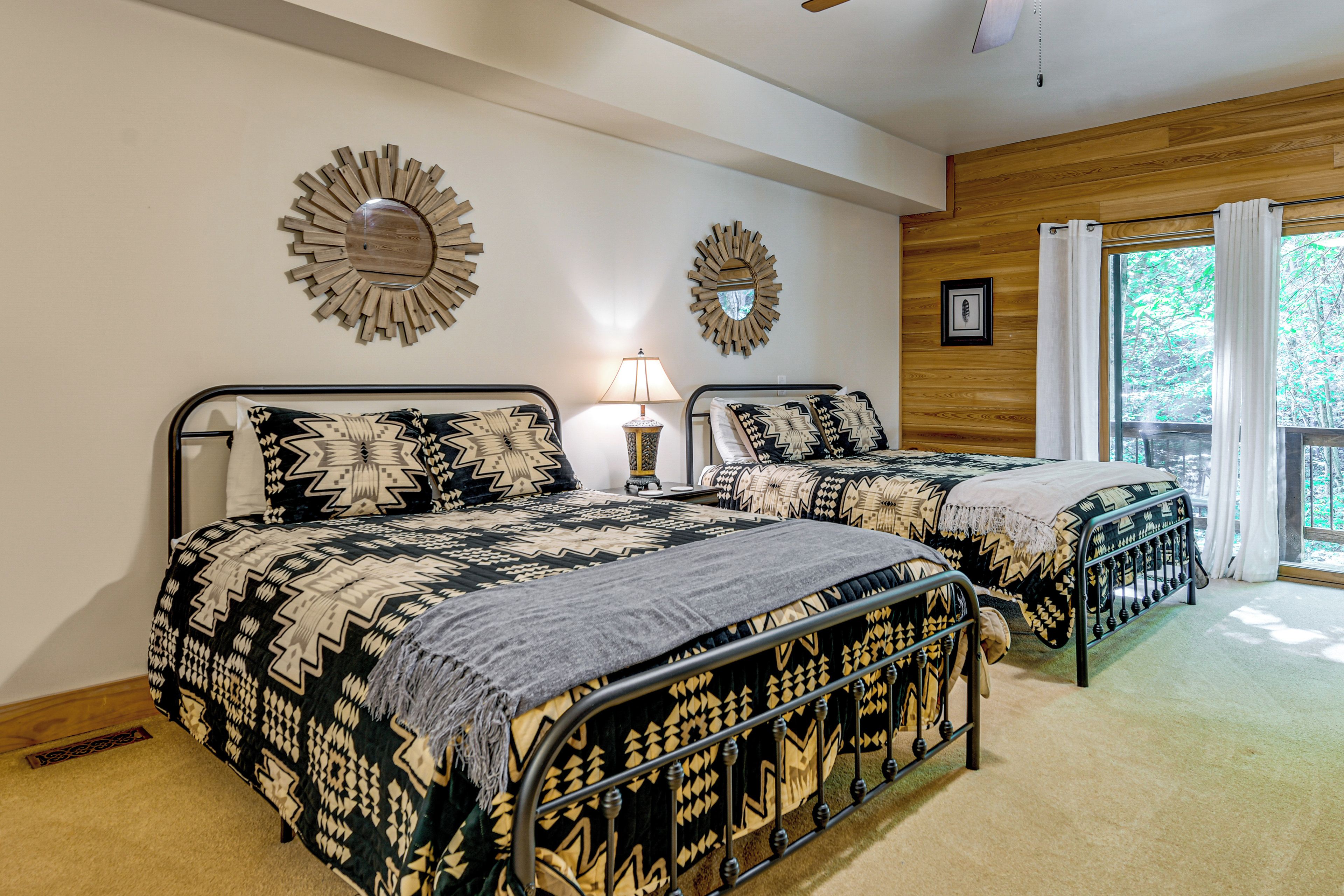 A bedroom with two beds, each with patterned bedding, a nightstand with a lamp, and decorative wall mirrors.