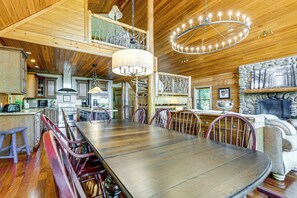 A spacious dining area with a long table and chairs, a chandelier, and a stone fireplace. - Panoramic Mtn Views: Luxe Cataloochee Cabin! (Waynesville)