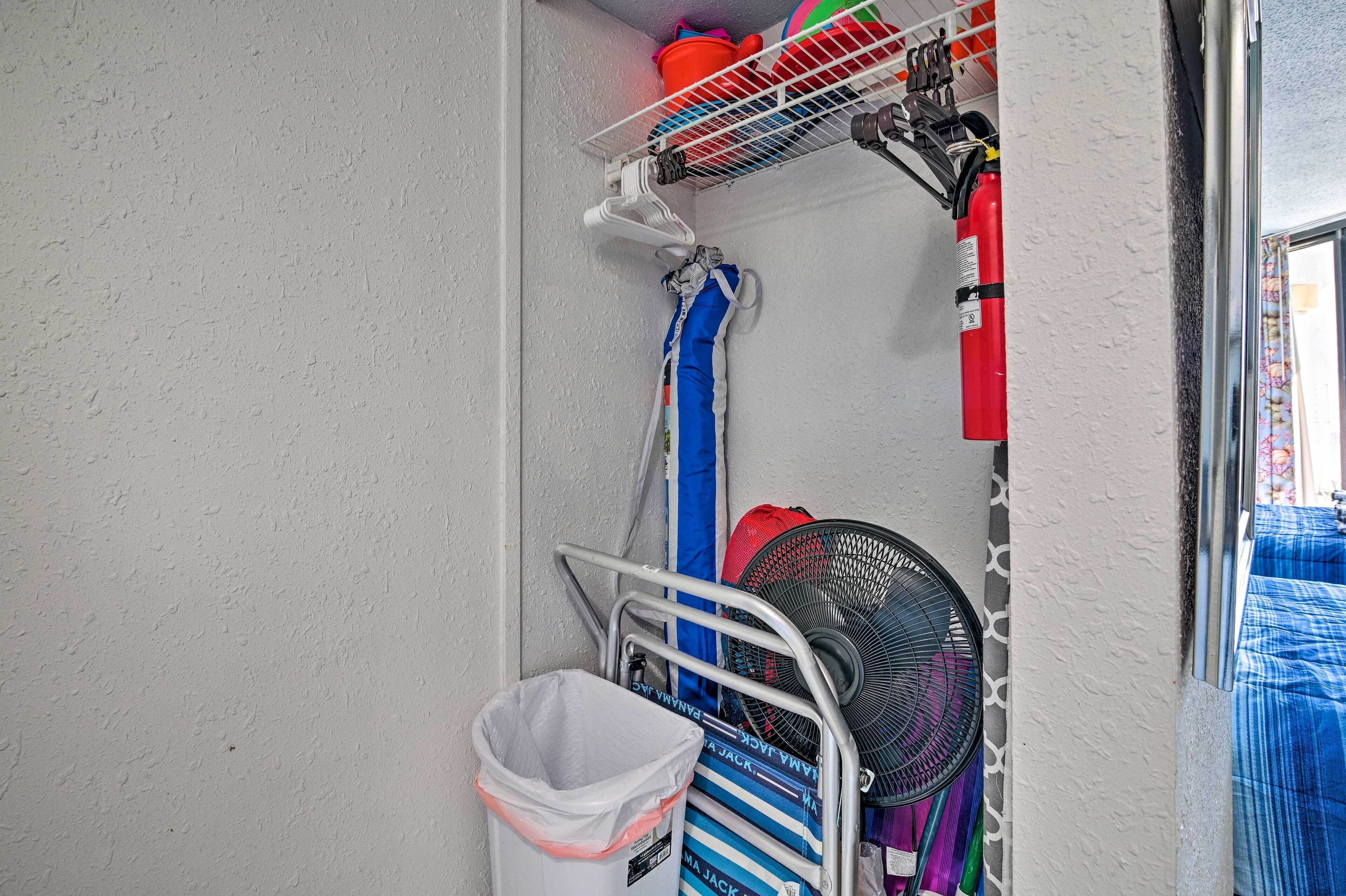 A corner of a room with a white textured wall, a metal rack with various items, a trash bin, and a window with a blue curtain.