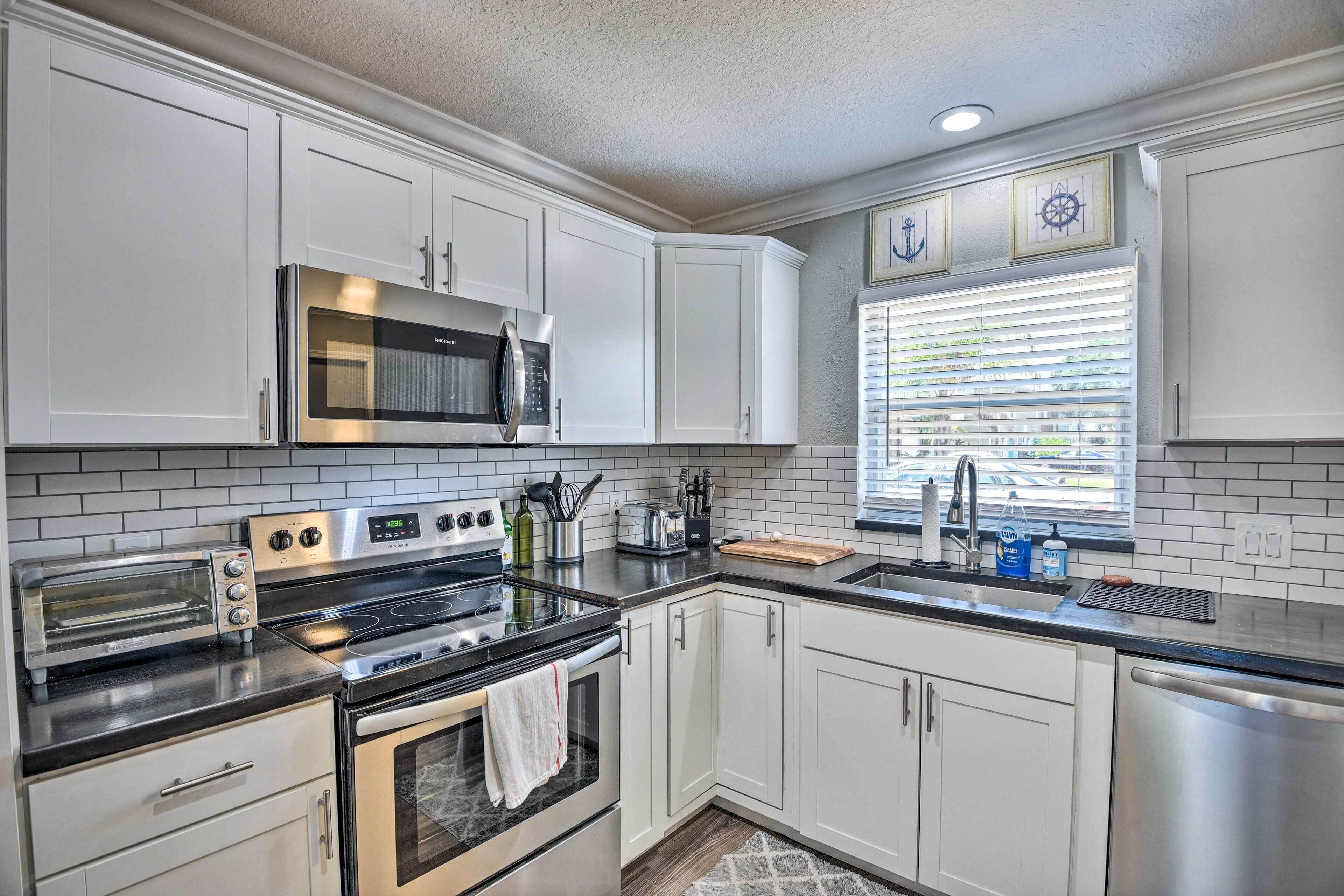 A modern kitchen with white cabinets, stainless steel appliances, and a window with blinds.