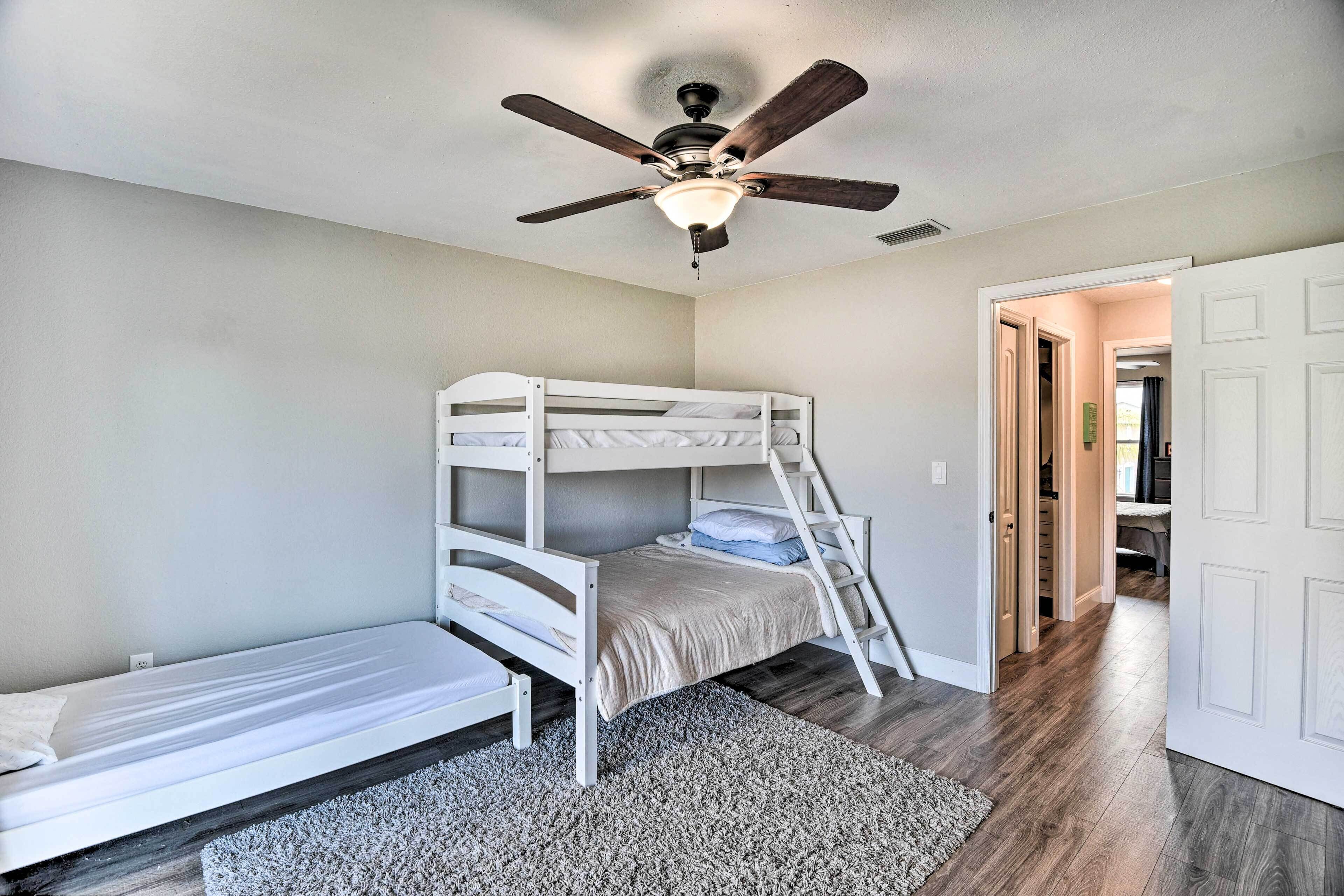 A bedroom with a bunk bed, a ceiling fan, and a door leading to another room.