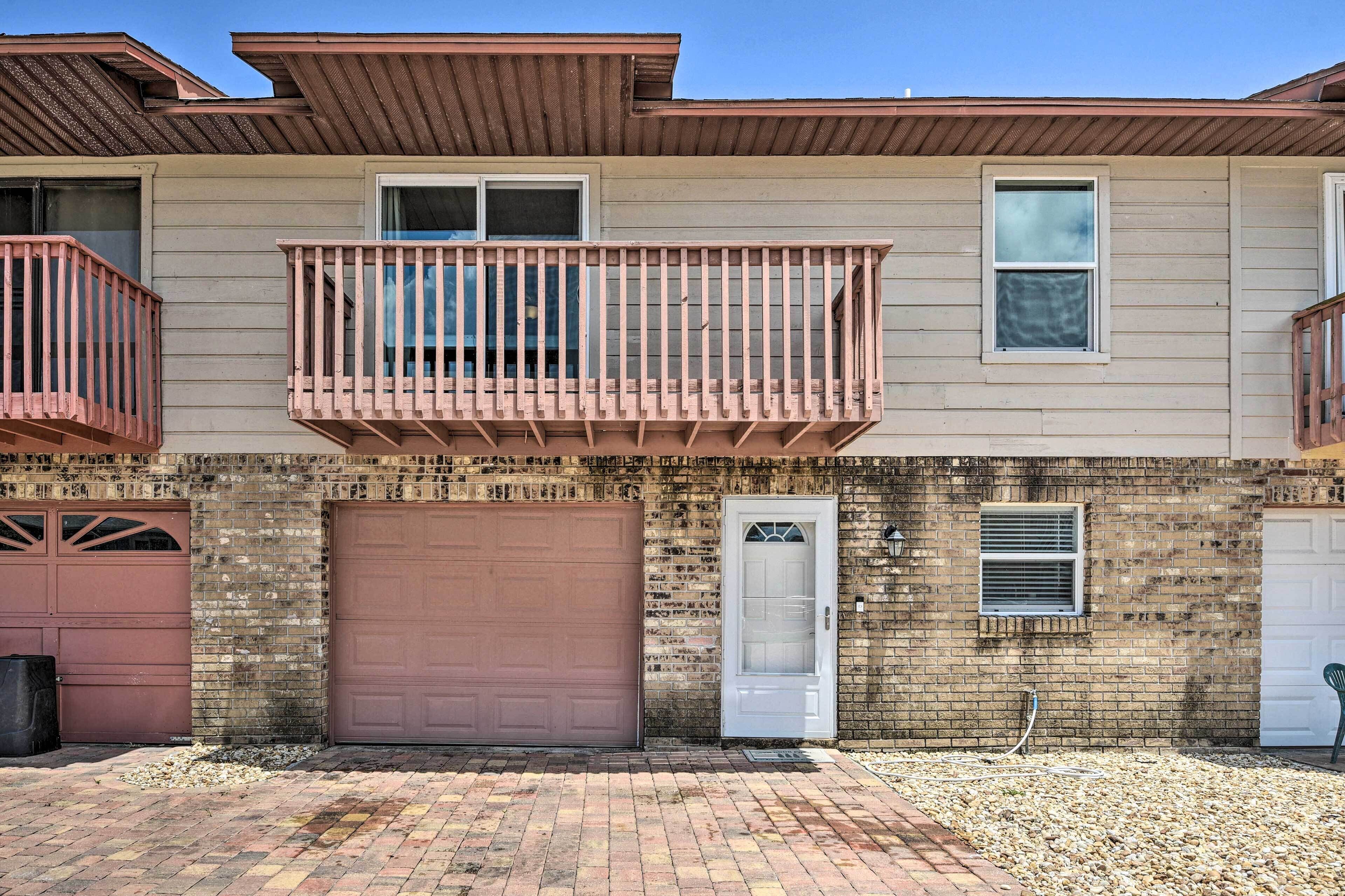 A two-story building with a brick facade, a brown garage door, and a small balcony with a metal railing.