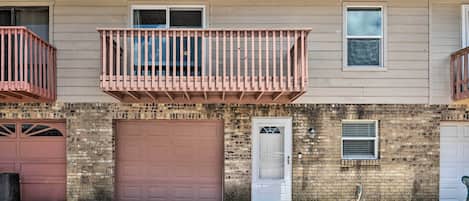 A two-story building with a brick facade, a brown garage door, and a small balcony with a metal railing.