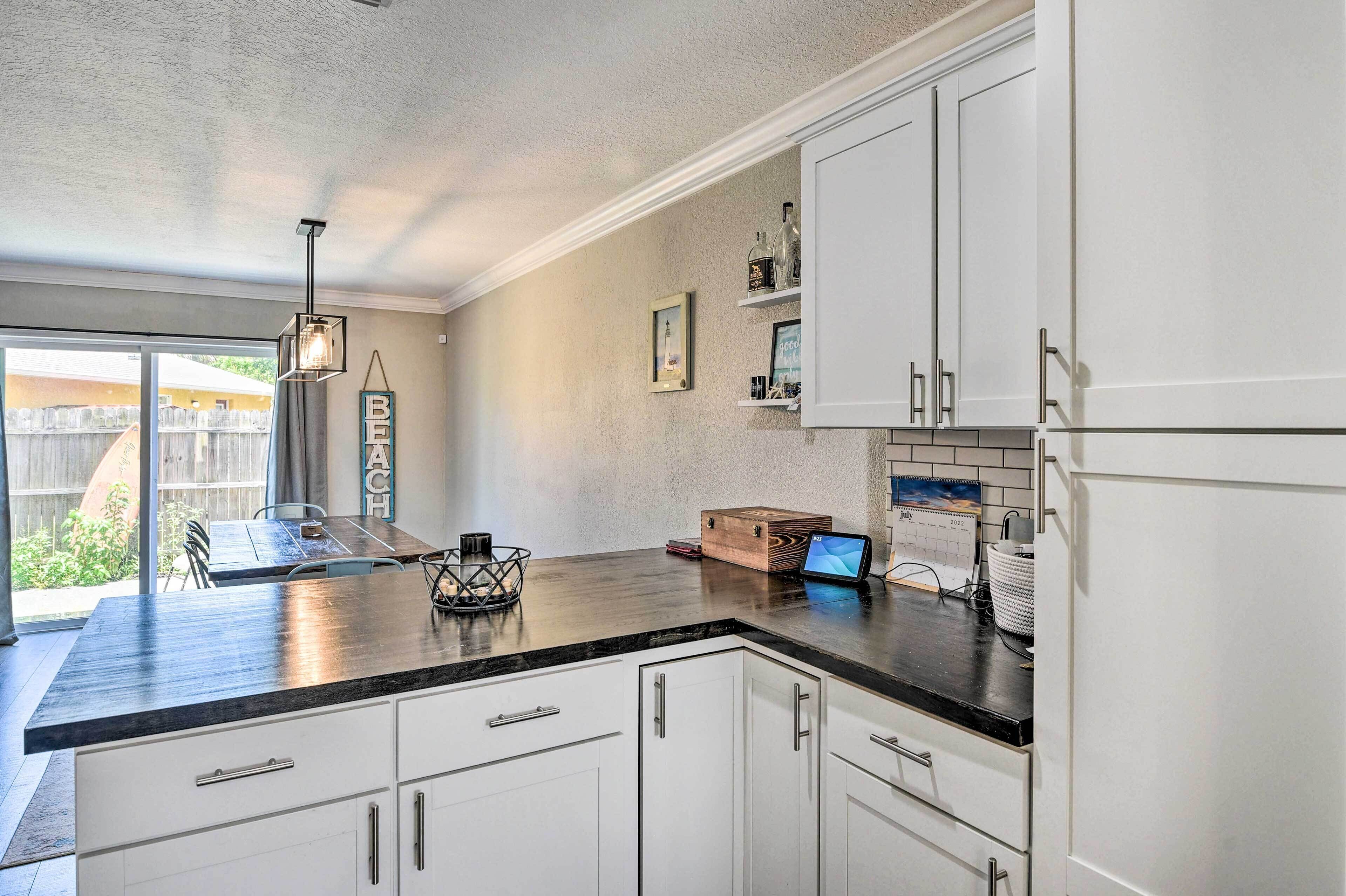 A modern kitchen with white cabinets, a black countertop, and a built-in refrigerator. There is a wooden box on the counter and a calendar on the wall.