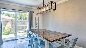 Un comedor con una mesa de madera y sillas azules, una lámpara colgante y un ventanal corredero que da a un patio trasero.