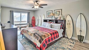 Un dormitorio con cama, escritorio, ventilador de techo y tablas de surf apoyadas en la pared.