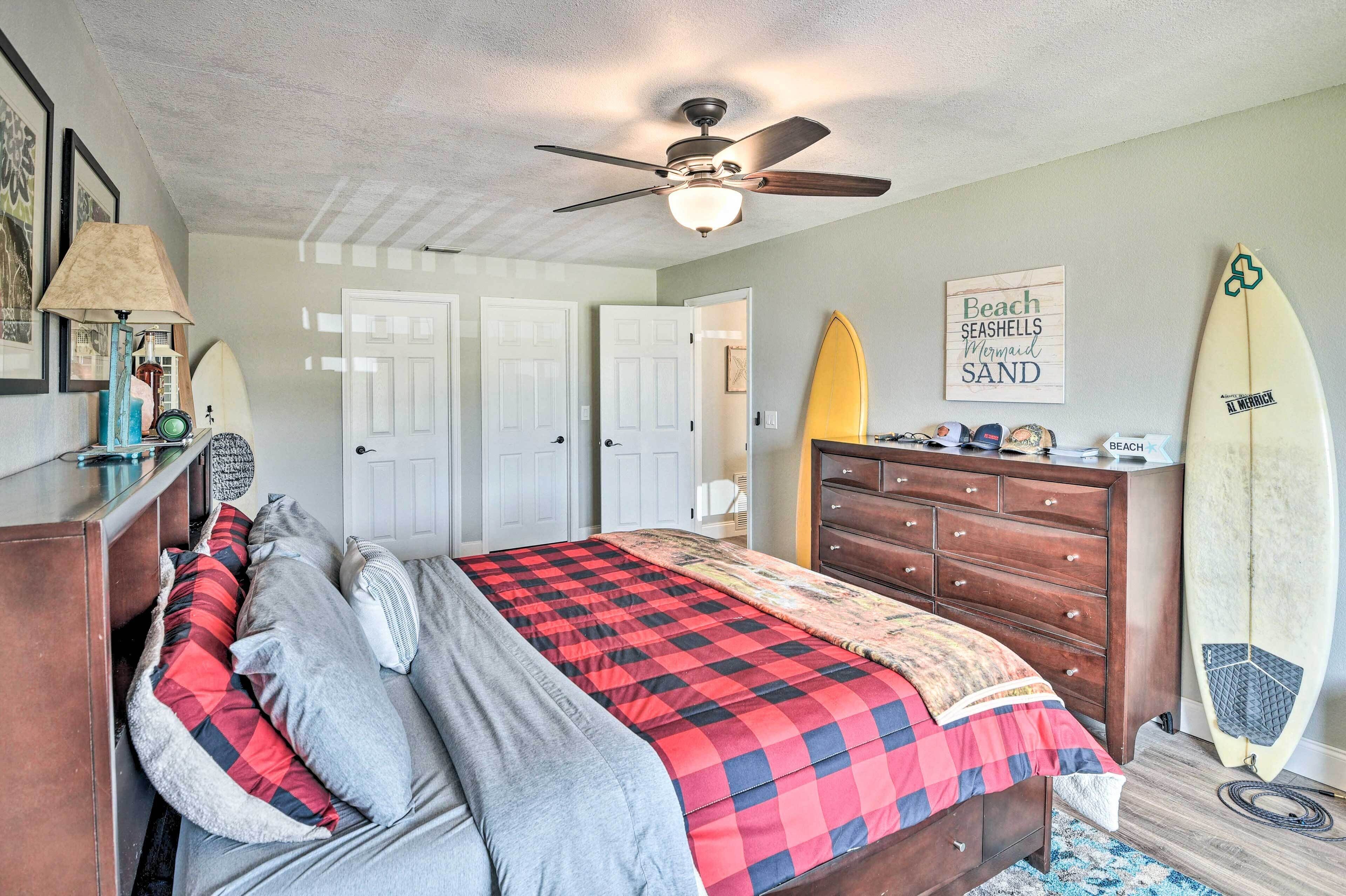 Quarto com cama, penteadeira, ventilador de teto e pranchas de surf.