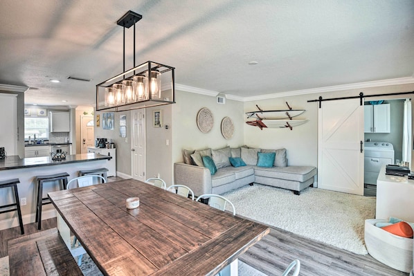 A modern kitchen with a dining area, a large wooden table, and a cozy seating area with a sofa and cushions.
