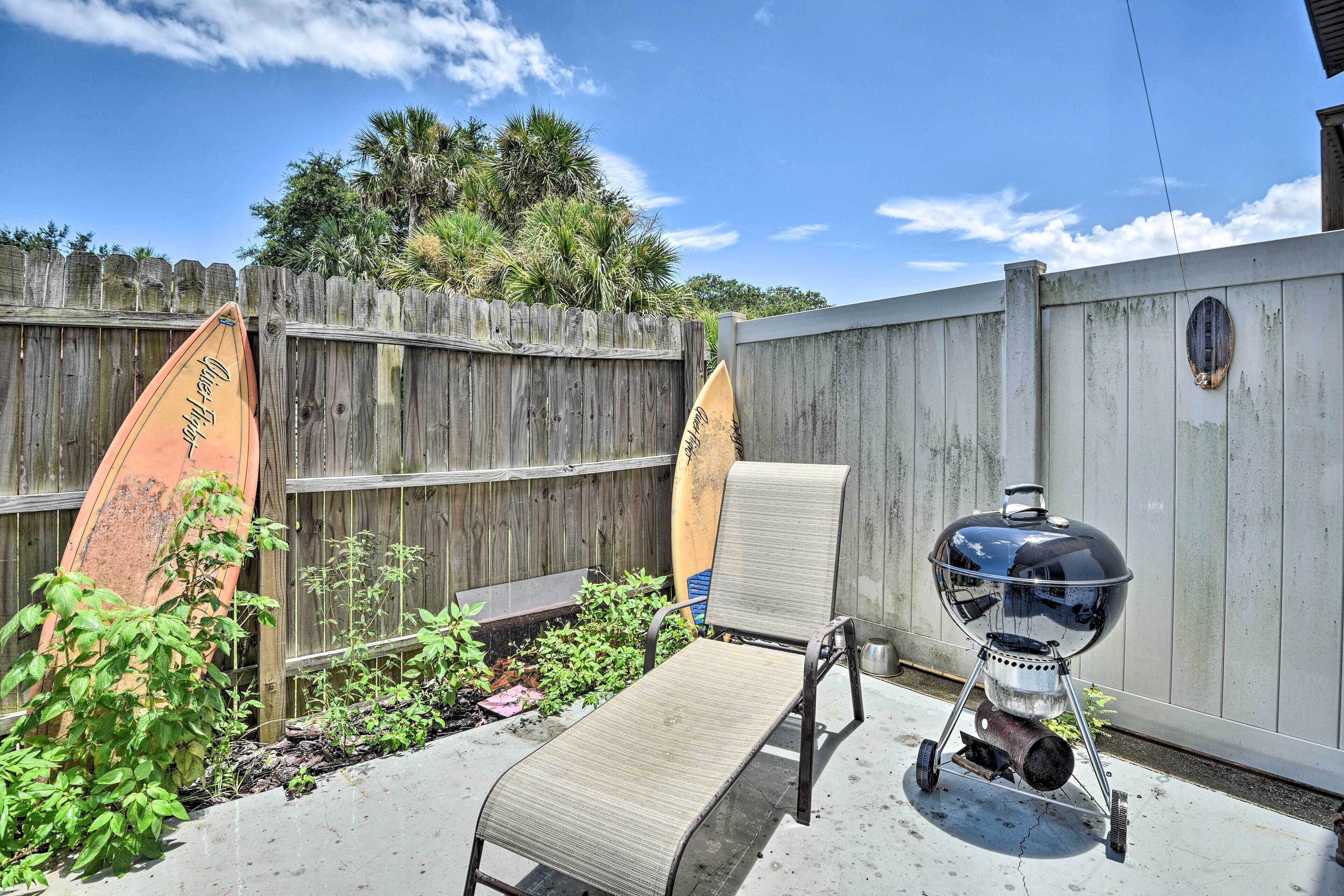A backyard with a wooden fence, a barbecue grill, and two surfboards leaning against the fence.