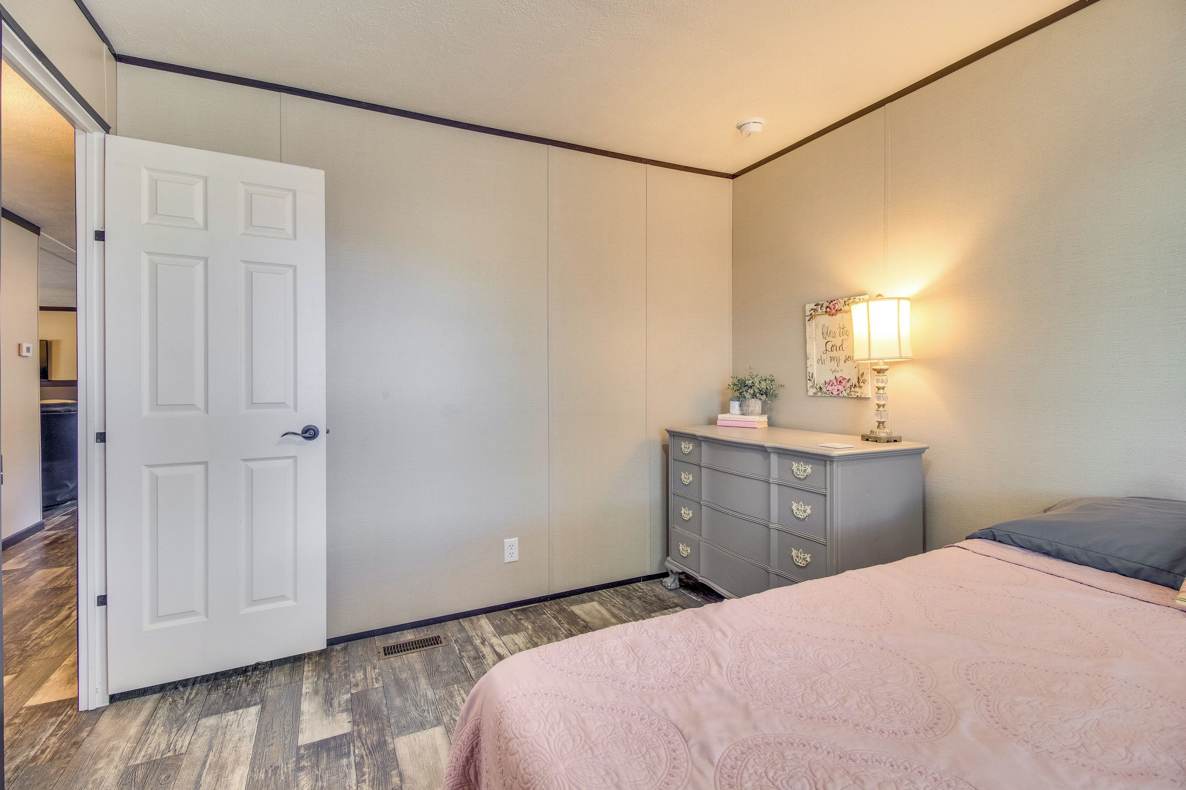 Une chambre à coucher avec un lit, une commode, une table de chevet, une lampe et une porte.