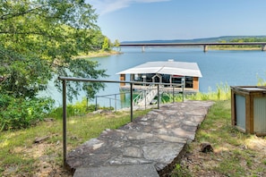 A stone pathway leading to a dock with a covered boat house, a metal railing, and a small shed by the water. - Greers Ferry Lakefront Home w/ Deck & Boat Slips! (Higden)