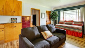 A cozy room with a dark brown sofa, wooden cabinets, a bed with a red bedspread, and a large window with curtains. - Spacious Wyoming Retreat: Fishing & Hunting (Torrington)