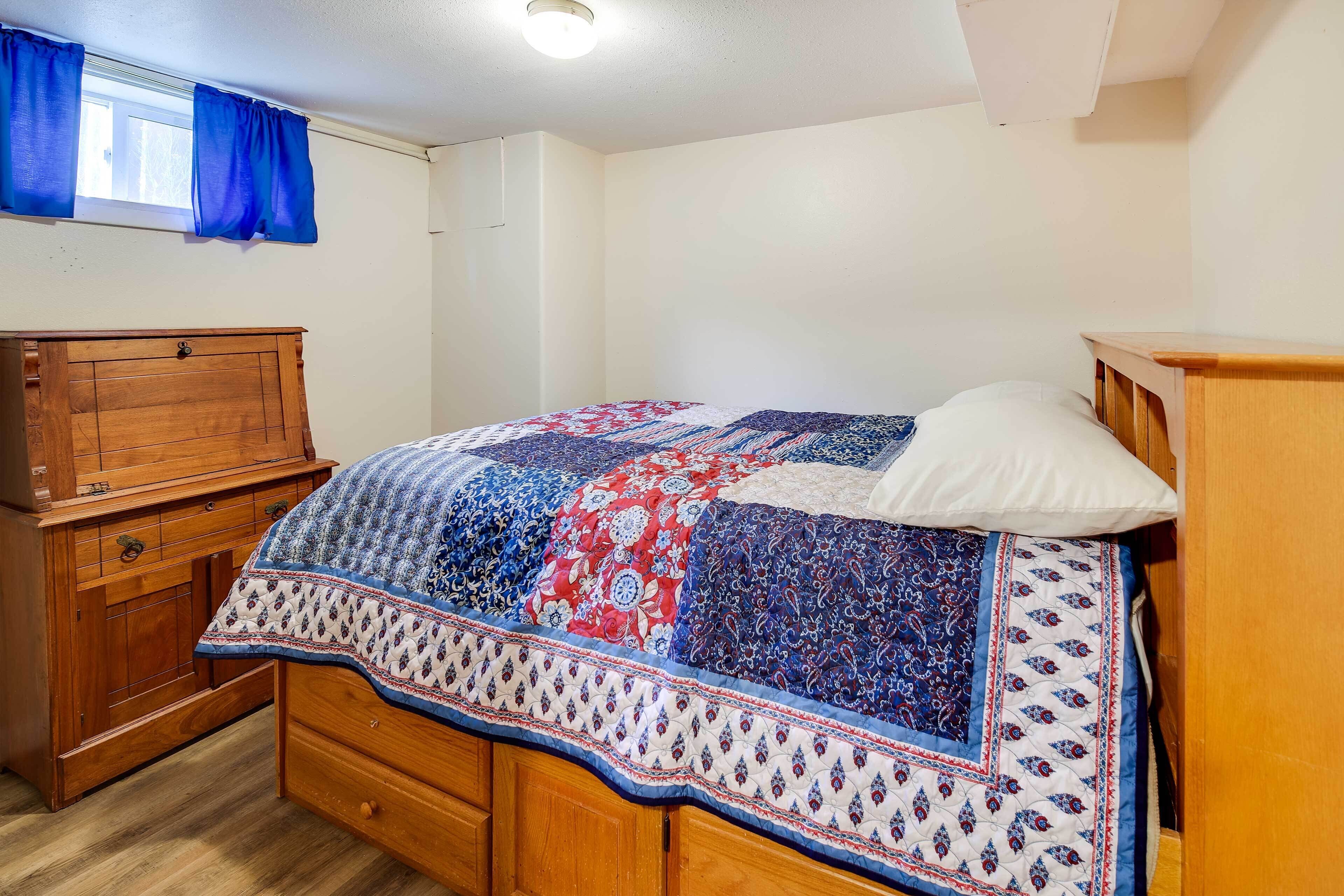 A bedroom with a wooden bed, a wooden dresser, and a window with blue curtains.