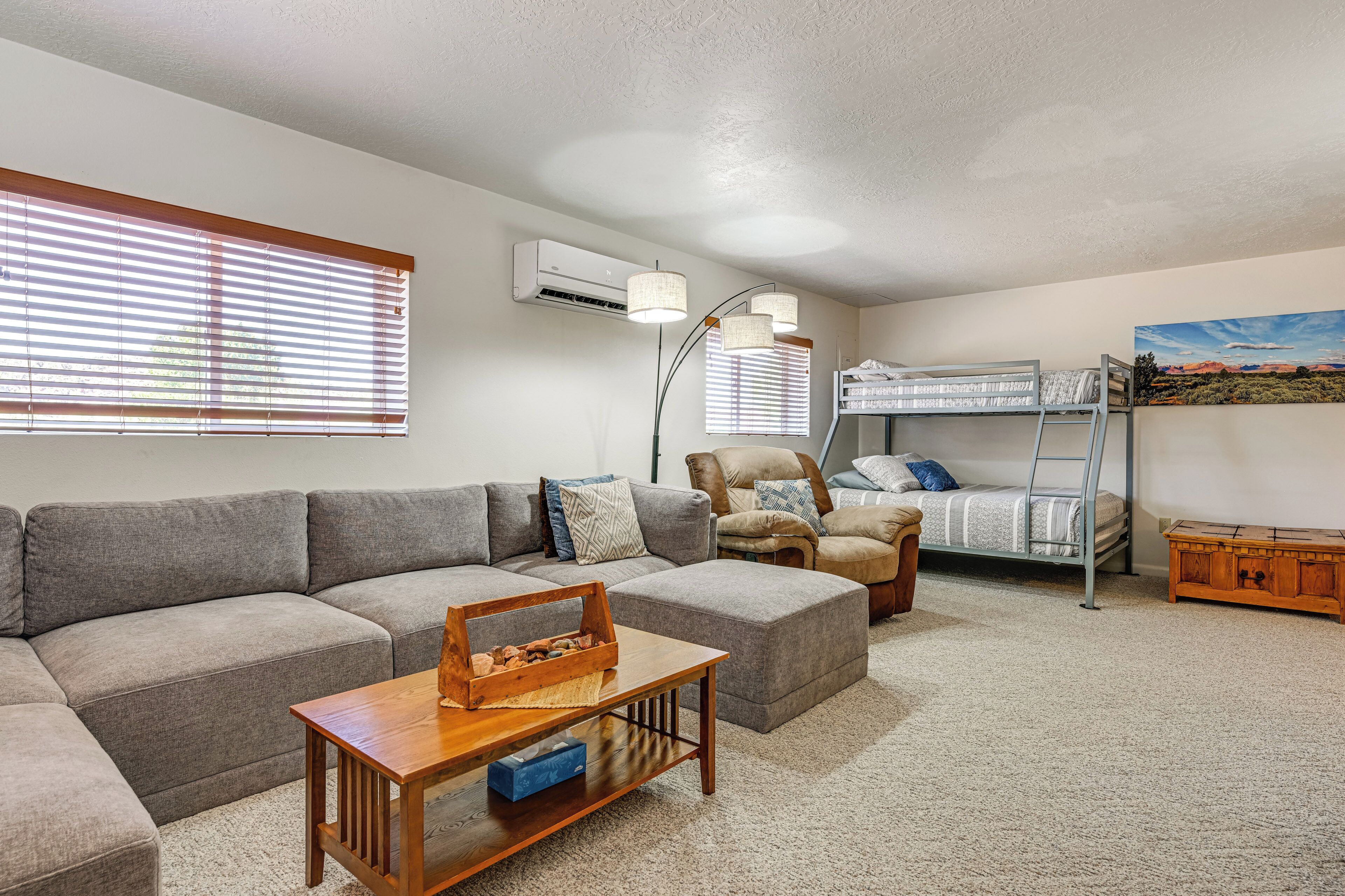 A cozy living room with a sofa, a coffee table, a bunk bed, a chair, and a painting on the wall.