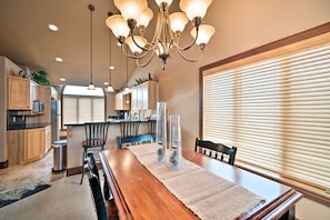 A dining area with a wooden table, chairs, a chandelier, and a kitchen in the background. - Cozy & Convenient Red Lodge Home < 8 Mi to Slopes! (Red Lodge)