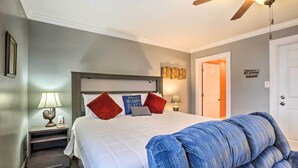 A bedroom with a bed, a nightstand, a lamp, a ceiling fan, and a door.
