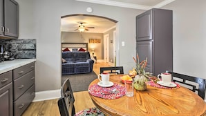 A dining area with a wooden table, two white cups, a pineapple, and a bowl of fruit.