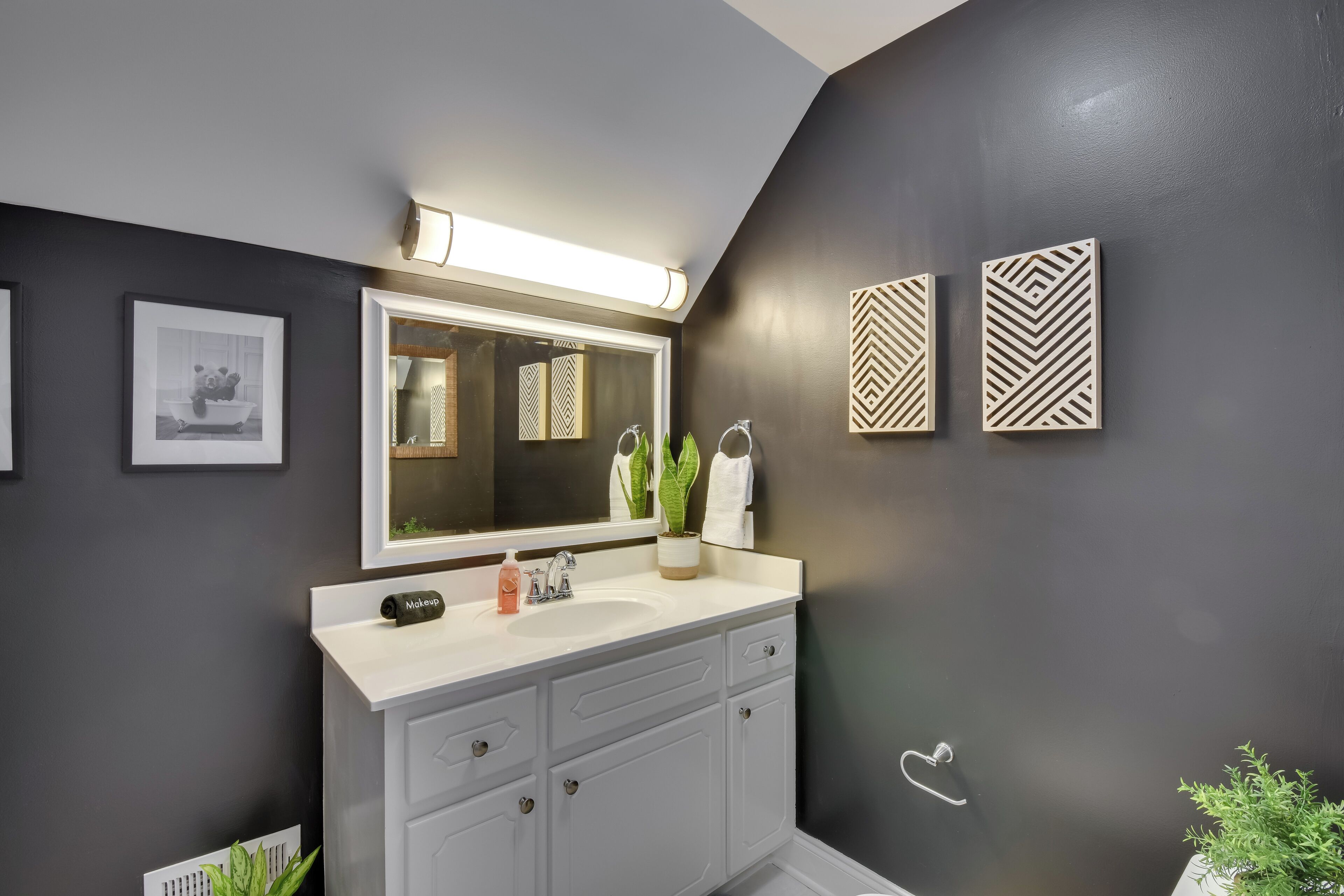 Un baño moderno con un espejo grande, tocador blanco y paneles decorativos en la pared.