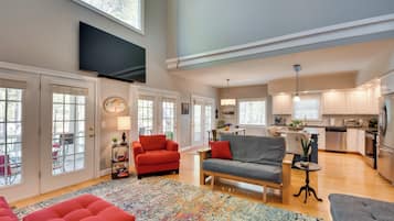 A spacious living room with a large TV, comfortable seating, and a view into the kitchen.