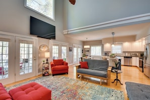 A spacious living room with a large TV, comfortable seating, and a view into the kitchen.