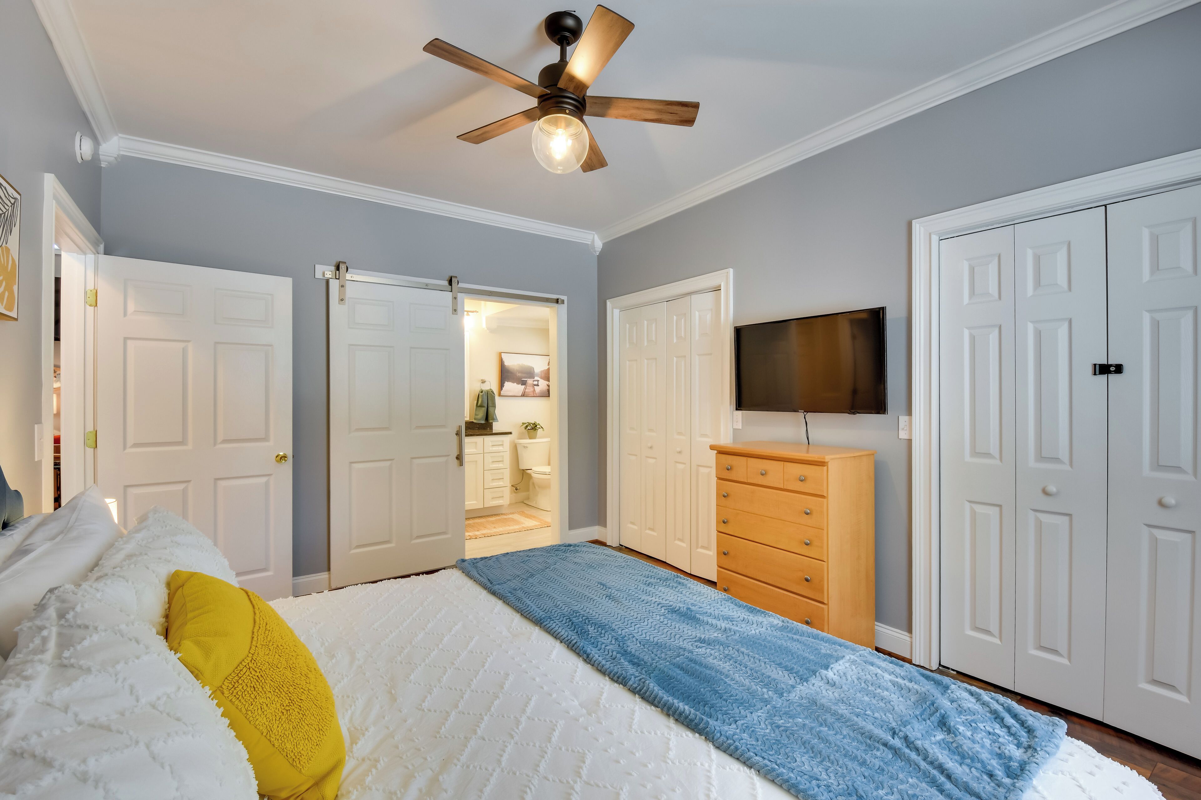 Ein Schlafzimmer mit Bett, Deckenventilator, Kommode, Fernseher und Kleiderschrank.