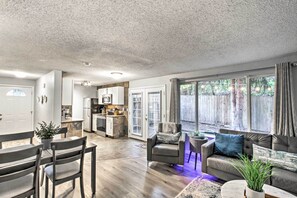A modern living room with a sofa, armchair, and dining table. There is a kitchen area with cabinets and appliances.